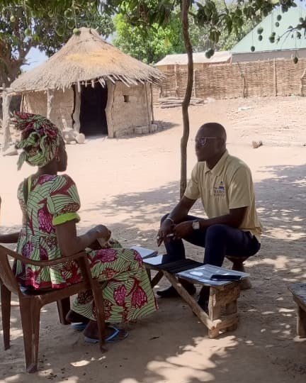 A KATS field interviewer conducts a structured interview with a community member outdoors.