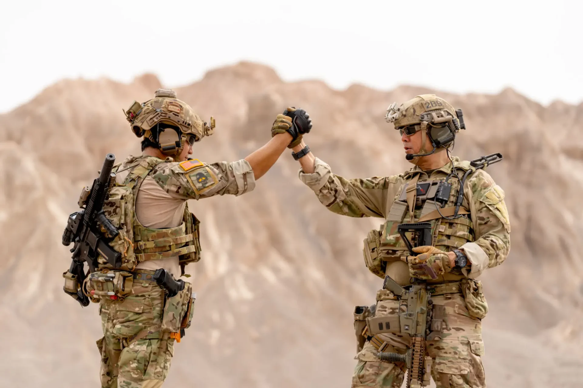 Two soldiers fist bumping in desert landscape.